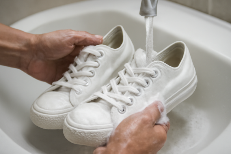 mains lavant une paire de sneakers blanches